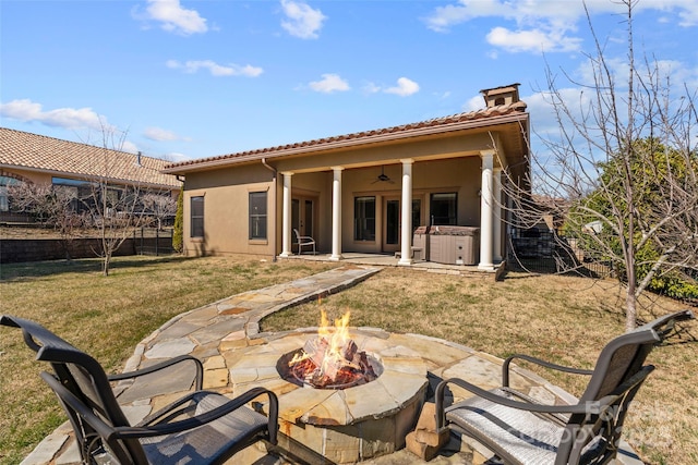 rear view of property with a patio, stucco siding, a lawn, a hot tub, and an outdoor fire pit