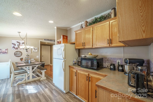 kitchen with crown molding, light countertops, hanging light fixtures, freestanding refrigerator, and black microwave