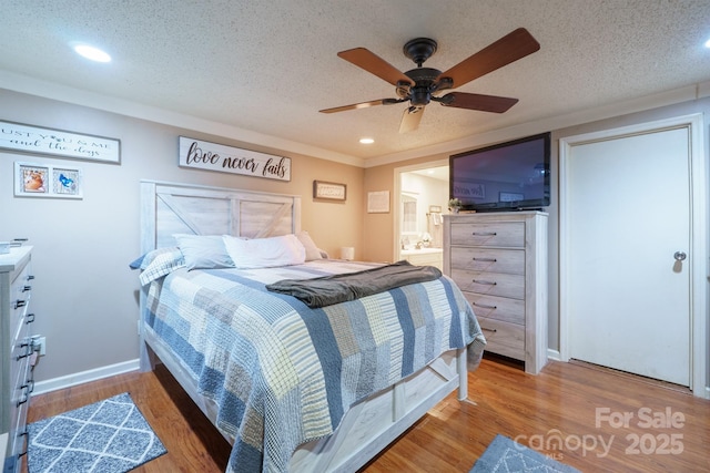 bedroom featuring a ceiling fan, a textured ceiling, ensuite bath, wood finished floors, and baseboards