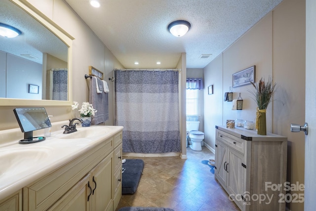 bathroom featuring double vanity, visible vents, toilet, a sink, and a textured ceiling