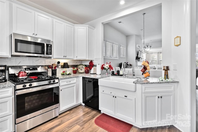 kitchen with a sink, white cabinets, appliances with stainless steel finishes, light wood-type flooring, and light stone countertops