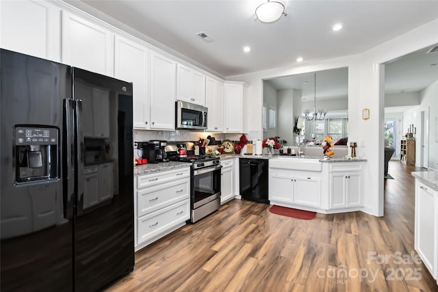 kitchen with light stone counters, visible vents, white cabinets, wood finished floors, and black appliances