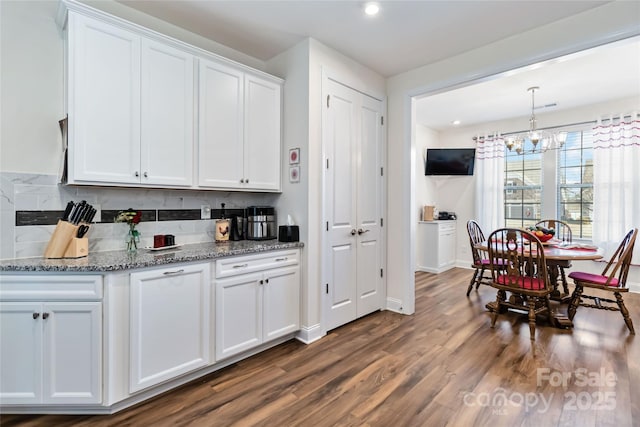 kitchen featuring light stone counters, dark wood-style flooring, decorative backsplash, white cabinetry, and a chandelier