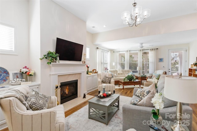 living area with ceiling fan with notable chandelier, a fireplace, and wood finished floors