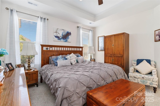 bedroom featuring carpet floors, a tray ceiling, visible vents, ornamental molding, and a ceiling fan