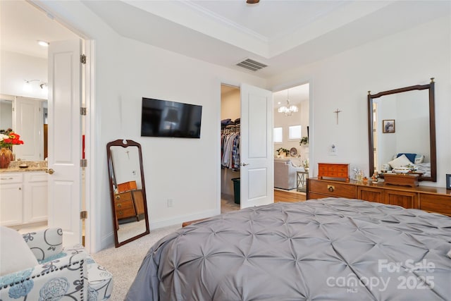 bedroom featuring ensuite bathroom, light carpet, visible vents, a tray ceiling, and a walk in closet