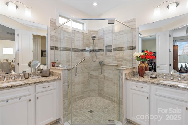 full bath featuring a shower stall, visible vents, two vanities, and a sink