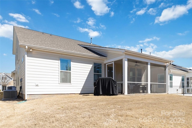 rear view of property with a yard, roof with shingles, central AC, and a sunroom