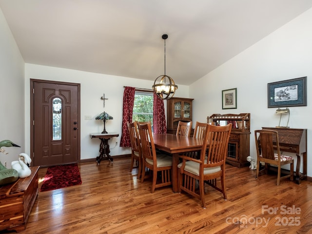 dining room featuring lofted ceiling, light wood finished floors, baseboards, and a chandelier