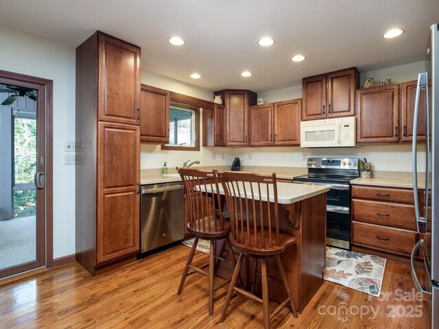 kitchen with recessed lighting, light wood-style floors, light countertops, appliances with stainless steel finishes, and a kitchen bar