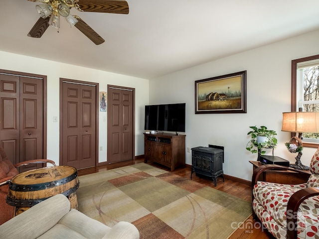 living room featuring light wood-type flooring, a wood stove, ceiling fan, and baseboards