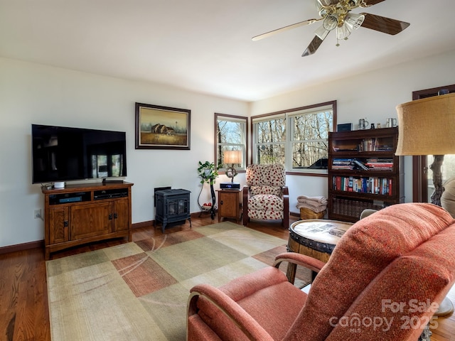 living room with a ceiling fan, wood finished floors, a wood stove, and baseboards