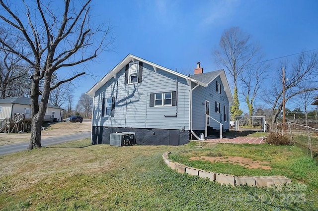 view of side of property with a lawn, a chimney, and central AC unit