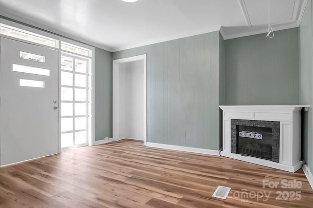 unfurnished living room featuring crown molding, a fireplace, visible vents, attic access, and wood finished floors