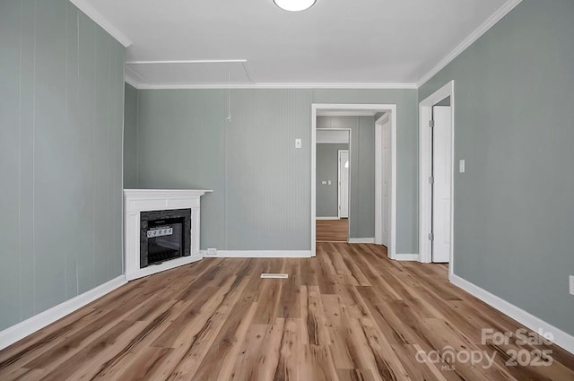 unfurnished living room with attic access, baseboards, a glass covered fireplace, wood finished floors, and crown molding