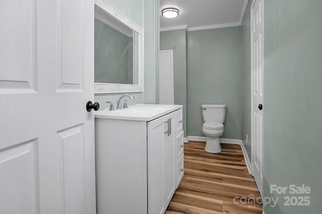 bathroom featuring baseboards, toilet, wood finished floors, crown molding, and vanity