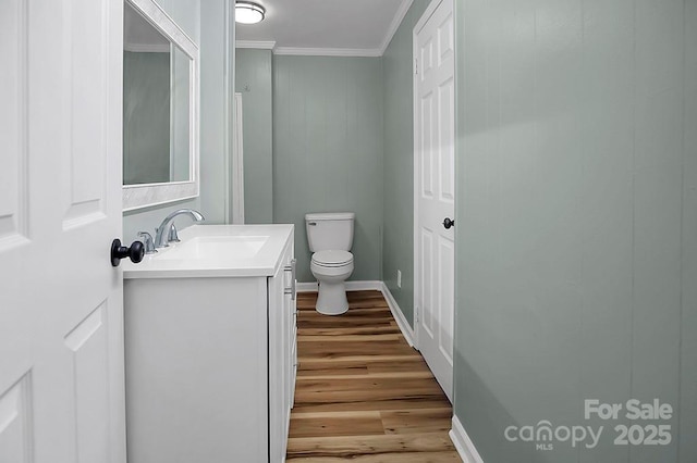 half bath with toilet, ornamental molding, vanity, wood finished floors, and baseboards