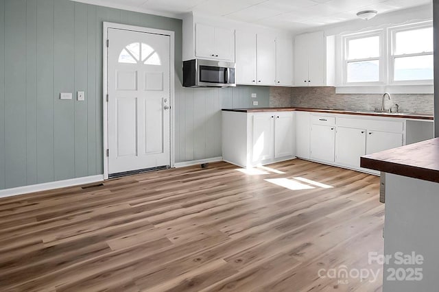 kitchen with butcher block counters, stainless steel microwave, light wood-style floors, white cabinetry, and a sink