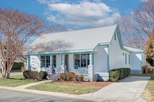 view of front facade featuring a shingled roof, a porch, and a front yard