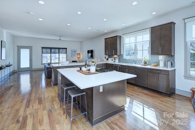 kitchen with a peninsula, dark brown cabinetry, light countertops, and a sink