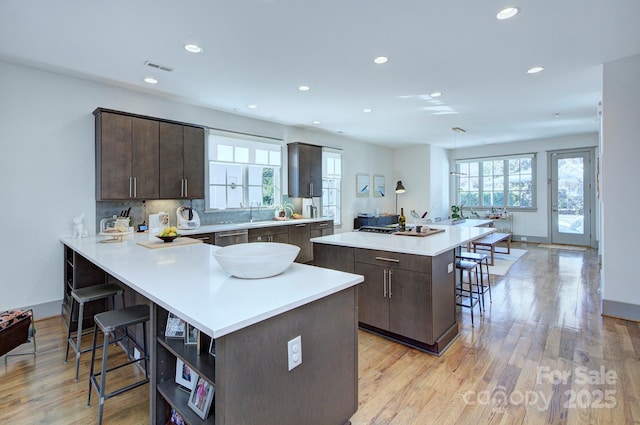 kitchen featuring dark brown cabinetry, a kitchen island, a breakfast bar area, and light wood finished floors