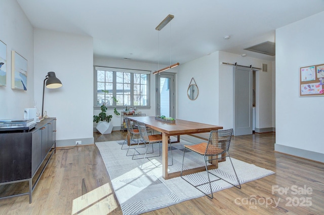 dining space featuring a barn door, baseboards, and light wood-style flooring