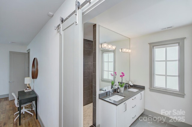 bathroom featuring double vanity, visible vents, a walk in shower, and a sink