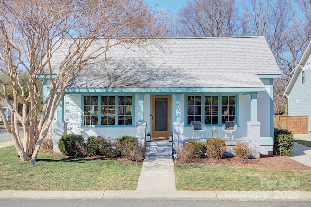 view of front of home featuring a shingled roof, fence, and a front lawn