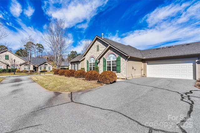 view of front of home with a shingled roof, stone siding, driveway, and a front lawn