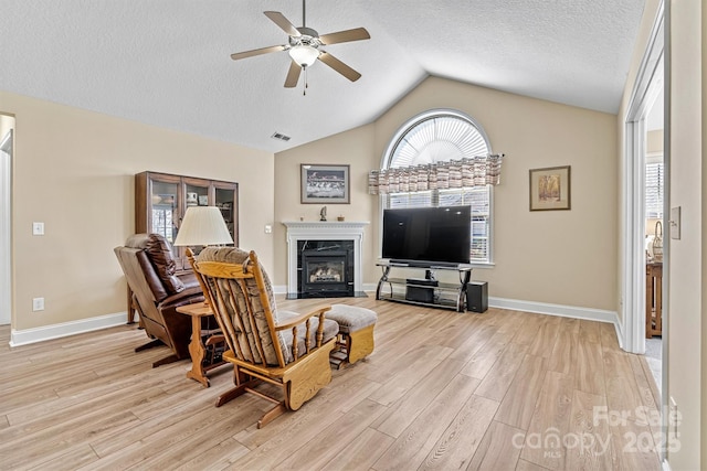 living room featuring ceiling fan, light wood-style flooring, a premium fireplace, vaulted ceiling, and a textured ceiling