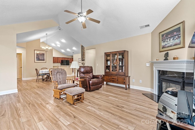 living room featuring visible vents, baseboards, lofted ceiling, light wood-style flooring, and a high end fireplace