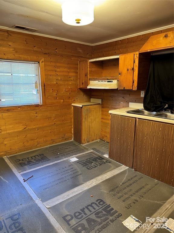 kitchen with wood walls, visible vents, brown cabinets, and ornamental molding