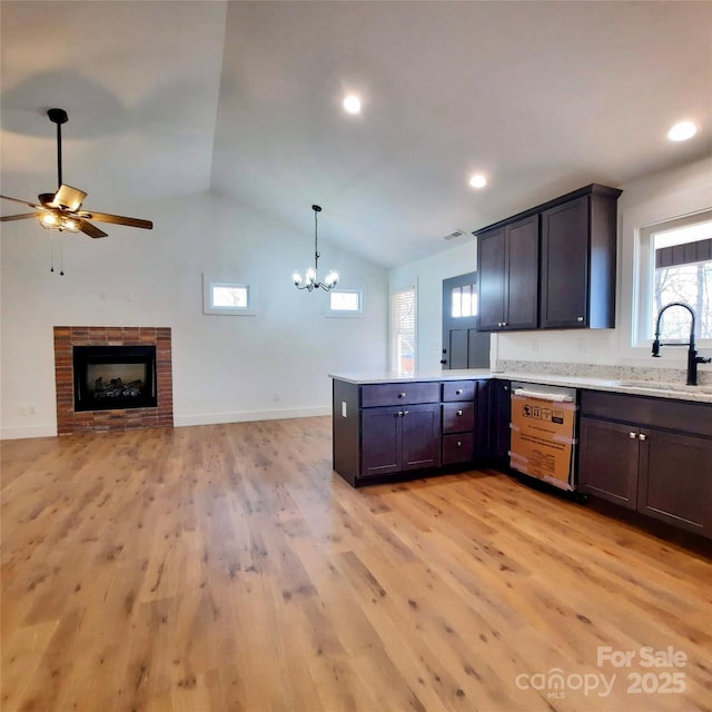 kitchen with dishwashing machine, a peninsula, light wood-type flooring, a brick fireplace, and a sink