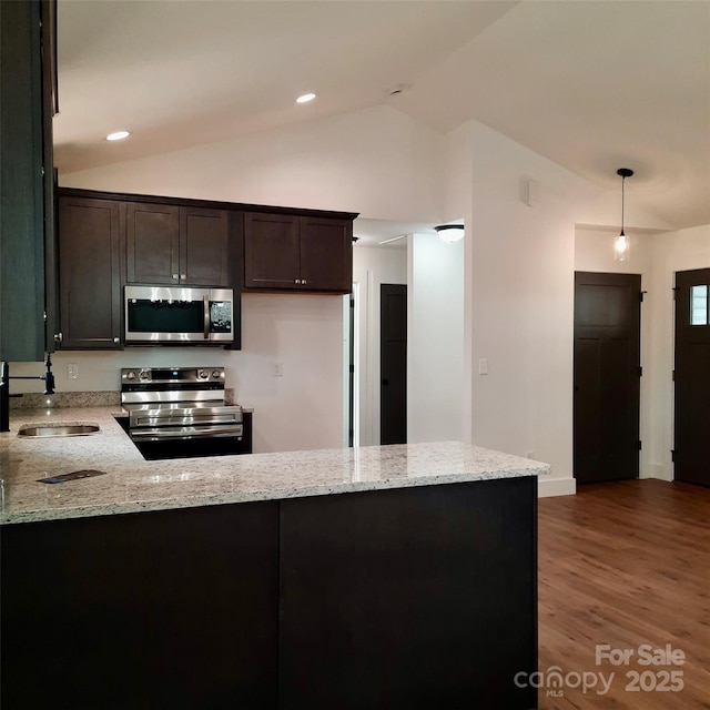 kitchen with light stone counters, lofted ceiling, appliances with stainless steel finishes, a sink, and a peninsula