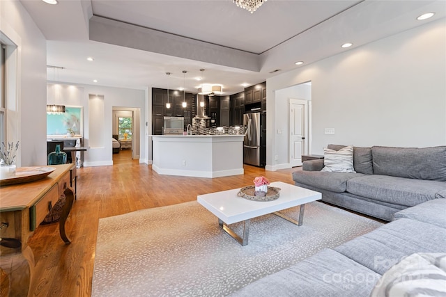 living area featuring light wood finished floors, baseboards, a raised ceiling, and recessed lighting