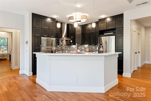 kitchen with tasteful backsplash, light countertops, visible vents, appliances with stainless steel finishes, and wall chimney range hood