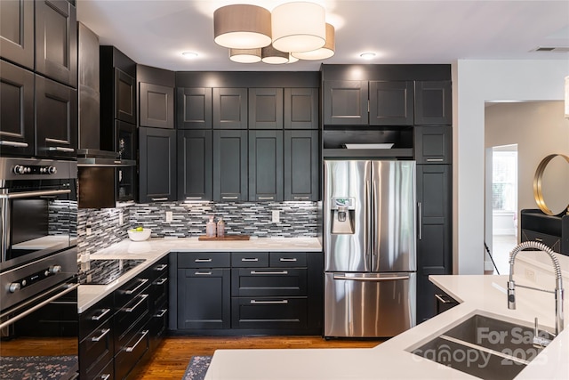 kitchen featuring stainless steel appliances, wood finished floors, a sink, light countertops, and backsplash