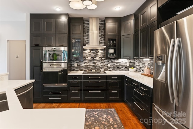 kitchen with stainless steel appliances, light countertops, backsplash, wall chimney exhaust hood, and dark wood finished floors