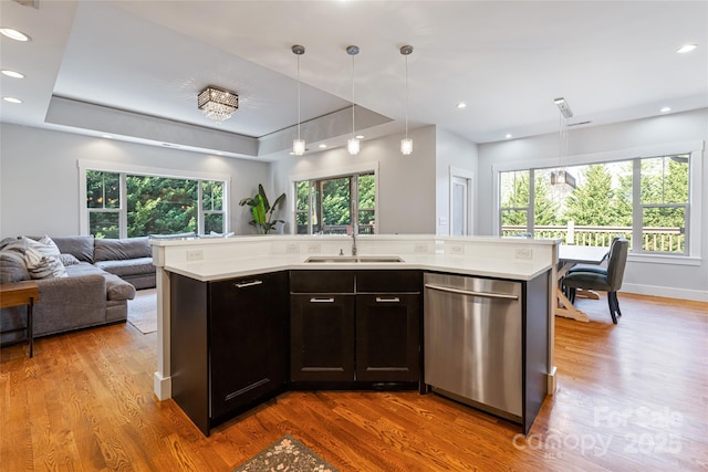 kitchen featuring a raised ceiling, light countertops, open floor plan, a sink, and dishwasher