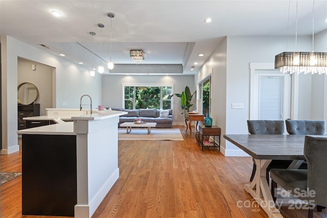 kitchen with decorative light fixtures, a sink, light countertops, light wood finished floors, and a center island with sink