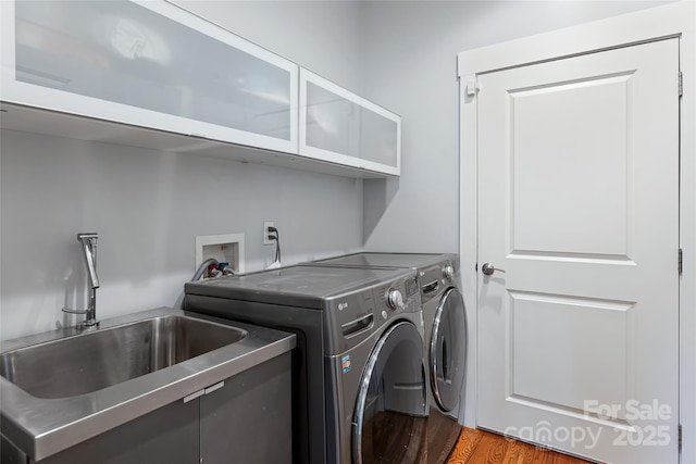 laundry area with wood finished floors, washer and clothes dryer, a sink, and cabinet space