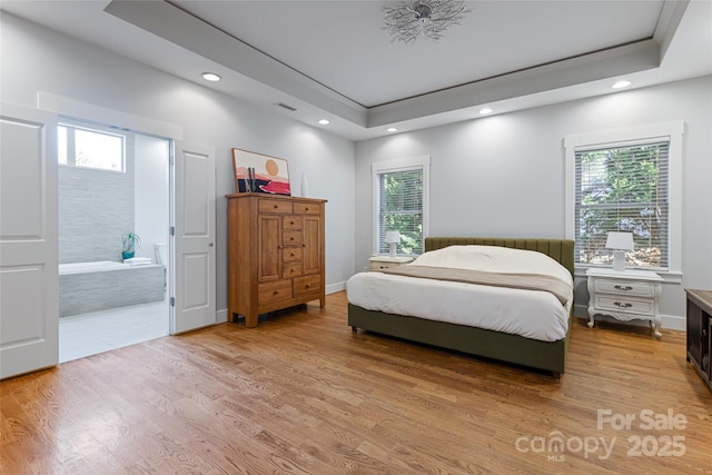 bedroom featuring multiple windows, light wood-type flooring, and a raised ceiling