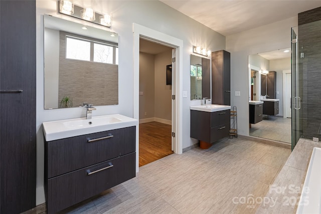 full bath featuring baseboards, two vanities, a sink, and a shower stall