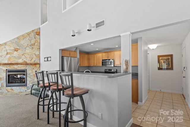 kitchen featuring a fireplace, light tile patterned floors, stainless steel appliances, a towering ceiling, and a kitchen bar