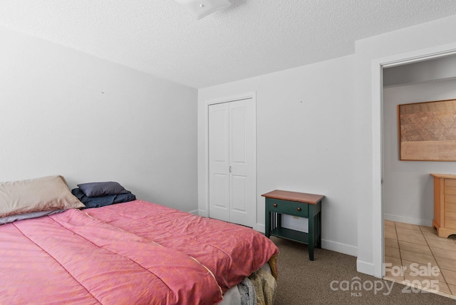 tiled bedroom with a closet, carpet flooring, a textured ceiling, and baseboards