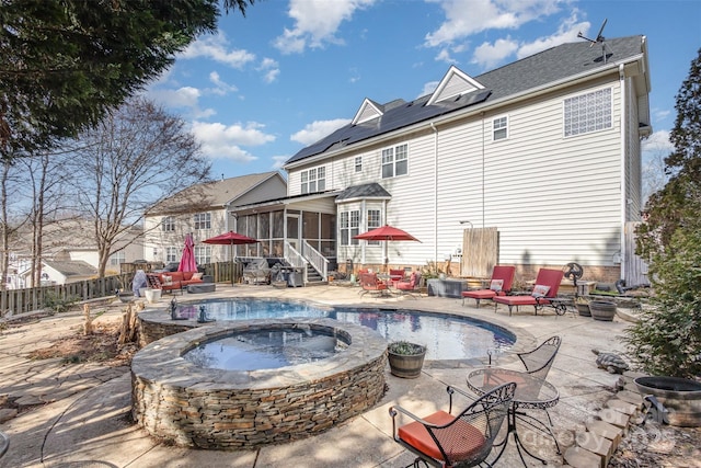 rear view of property with a fire pit, a sunroom, a patio area, and roof mounted solar panels