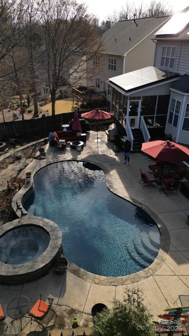 view of swimming pool featuring a pool with connected hot tub, an outdoor fire pit, a sunroom, a patio area, and fence