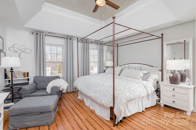 bedroom with light wood-style floors, a tray ceiling, and ornamental molding