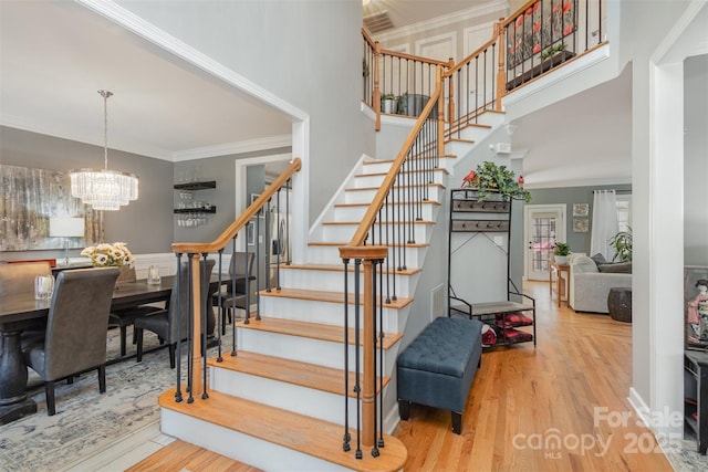 stairs featuring a notable chandelier, a high ceiling, ornamental molding, and wood finished floors