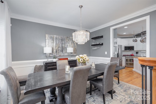 dining room featuring a wainscoted wall, light wood-style flooring, wine cooler, crown molding, and a notable chandelier